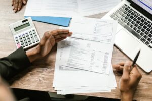 Laptop z systemem KSeF na biurku biurowym, dokumenty dotyczące kontroli obowiązków podatków i compliance, naturalne oświetlenie z okna